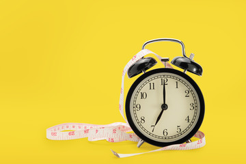 alarm clock with measuring tape isolated on yellow background, diet concept