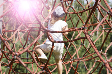 Active young girl climbing the spider web playground activity in summer.