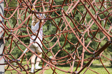 Active young girl climbing the spider web playground activity in summer.