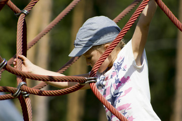 Active young girl climbing the spider web playground activity in summer.