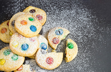 Chocolate chips and multicolored candy homemade shortbread cookies icing powdered on gray background. Selective focus.