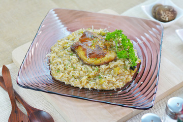 Risotto foie gras (Fried rice Italian style) in glass square plate on wood cutting board.