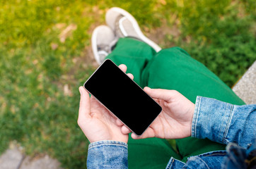 Man use his Mobile Phone outdoor, close up. Mobile phone in hands a young hipster business man in denim shirt and green jeans on the background of green grass.