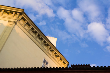 Obraz premium Detail of architecture - top of the building with decorated ledge. Blue sky with clouds as copy space. Corrugated pattern of roof tiles at the bottom