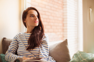 The young beautiful woman lying on sofa in the room and looking in the window