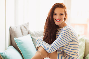 Naklejka premium The young joyful woman sitting on the sofa in the room and smiling