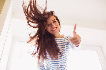 Portrait of young beautiful woman who smiling and showing thumb up in the room