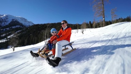 happy mom with baby son sledging down snow sled run on sunny winter day
