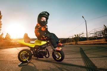 Child on a motorcycle doing moto stunt. Small boy get a difficult and dangerous trick on his small motorcycle. Small biker dressed in a protective suit and helmet.