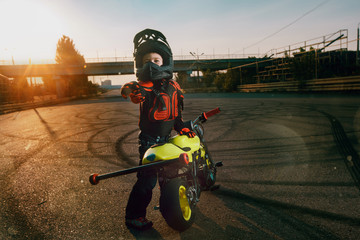 Child on a motorcycle doing moto stunt. Small boy get a difficult and dangerous trick on his small motorcycle. Small biker dressed in a protective suit and helmet.