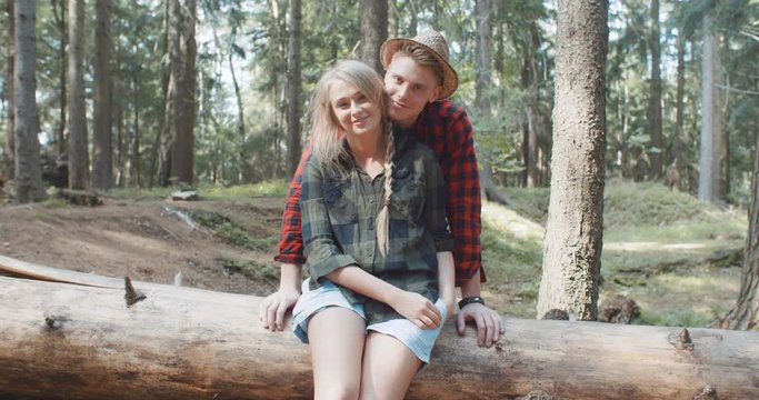 Portrait of beautiful caucasian couple spending time in a forest during sunny day. Smiling friends looking at camera in the woods.