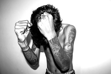 A young man without a shirt, with his hands full of tattoos. High Key Photo with black and white filter color. 