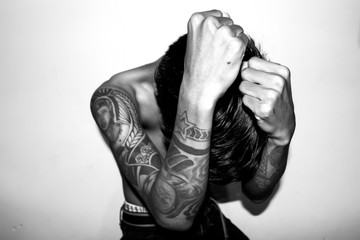 A young man without a shirt, with his hands full of tattoos. High Key Photo with black and white filter color. 