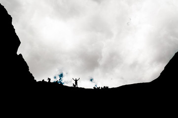Silhouette of man standing on top of the hill with raised hands.