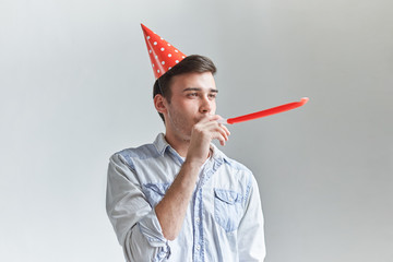 Studio shot of unshaven young Caucasian male blowing whistle while celebrating his friend's...