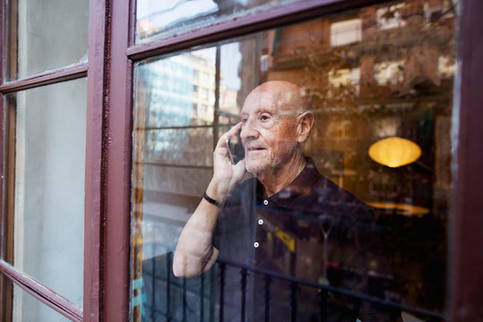 Elderly man looking through the window talking on phone.