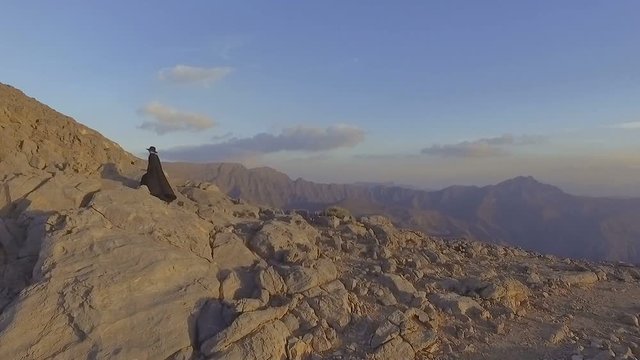 Dark witch young woman with isis wings climbs uphill. Girl in zorro costume is walking in the jebel jais mountains waving cloak. Mystic lady dreams about freedom, game of thrones style. Slow motion