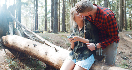Loving young caucasian couple spending time in a forest. Man and woman on vacation watching photos on their smartphone.