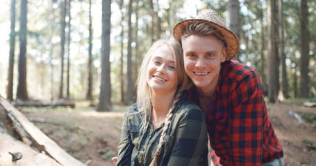 Portrait of beautiful caucasian couple spending time in a forest during sunny day. Smiling friends looking at camera in the woods.