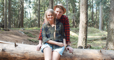 Portrait of beautiful caucasian couple spending time in a forest during sunny day. Smiling friends looking at camera in the woods.