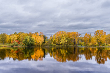 Fototapeta na wymiar The lake, reflecting the cloudy sky and autumnal foliage trees