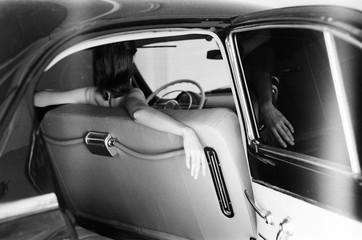 A black and white back portrait of a young woman seating in the retro car