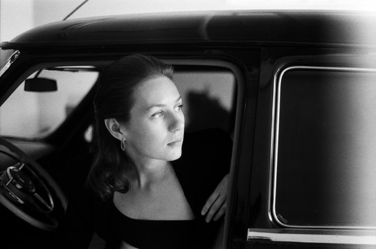 A black and white film portrait of a young woman seating in the retro car