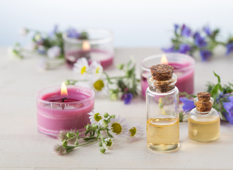 Plakat Essentials oils, burning candles and grass blossoms on white wooden table