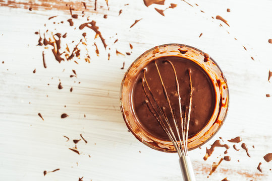 Chocolate ganache is prepared with raw chocolate and cream milk, on a glass containet with handmixer over a white background, backlighted with natural light.