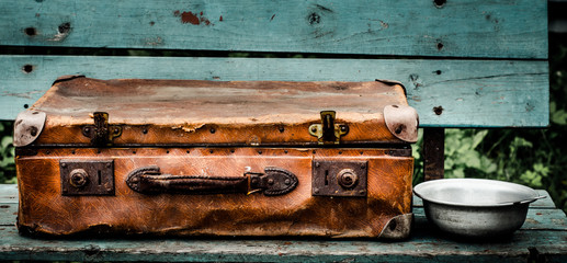 Vintage suitcase is lying on the bench. Next to the suitcase is metal plate.

