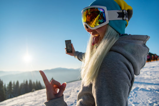 Female snowboarder enjoying sunset after snowboarding, using her smart phone, taking pictures of winter nature in the mountains copyspace connectivity mobility freeride lifestyle concept