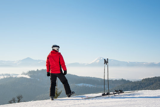Rearview shot of a skier resting after the ride standing on top of the ski slope looking around enjoying breathtaking view of snowy mountains on a sunny winter day seasonal recreational extreme active