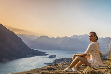 Naklejka na ściany i meble девушка сидит на обрыве скалы с видом на залив и горы в Черногории