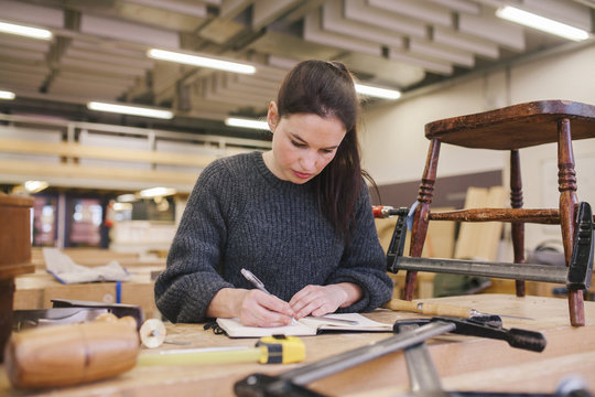 Female woodworker working on a bench, drawing her design before starting to work