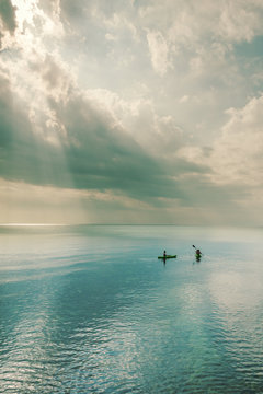 teen girls kayaking in the ocean with amazing sun rays through the clouds