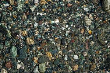 small multicolored stones on the bank of a mountain stream with crystal clear glacial water. Top view.