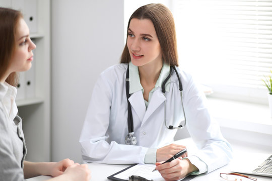 Female doctor having a talk with her patient  while sitting at the table near the window in hospital. Physician is ready to help patient. Medicine and health care concept