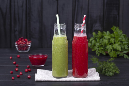 Two glass bottle of juice smoothie shake from green parsley, dill, broccoli, avocado and red cranberry on black wooden background, close up