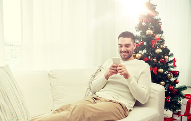 smiling man with smartphone at home for christmas