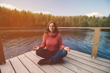 girl in sweater sitting on the pier in the park and meditating