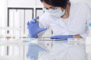 Close-up of professional female scientist in protective eyeglasses making experiment with reagents...