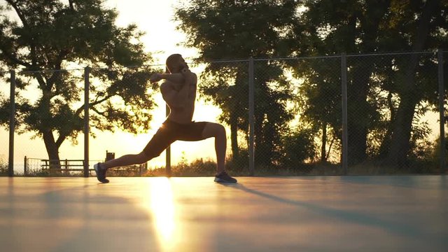 in slow motion view of strong muscular bearded guy training making exercises on basketball court with the sunlight on background