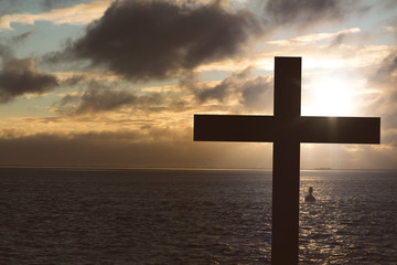 christian cross silhouette with sunset over the sea