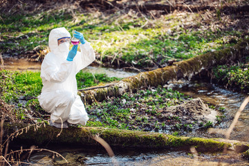 female scientist examining the liquid contents of a  test tube in the forest. Ecology and environmental pollution concept..