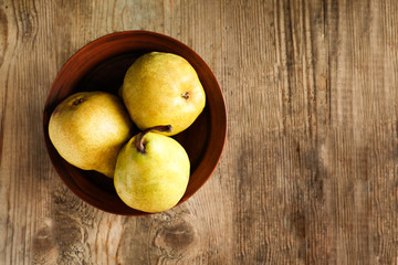 Ripe pears in bowl on wooden table