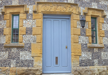 Fototapeta premium Light blue wooden doors to an old stone building with an office sign above.