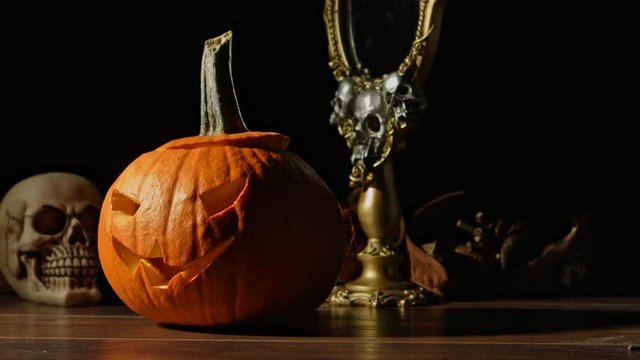 Carved Halloween pumpkin lights inside with flame and skuls around.