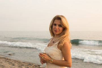 Fototapeta na wymiar Beautiful blonde lady with a glass of pink wine by seaside 