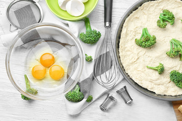 Uncooked broccoli quiche and ingredients on wooden table