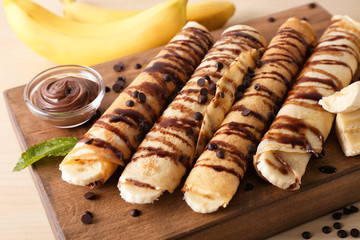 Delicious pancakes with chocolate sauce and banana on wooden board